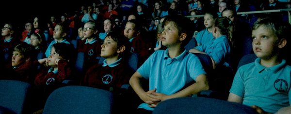 Digital Teach Dark auditorium, audience of school children are watching something unseen on stage or screen