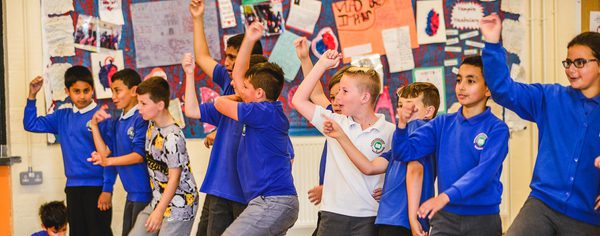 WNO Schools Workshops Kirsten McTernam A gruup of school children arms raised in play or performance.