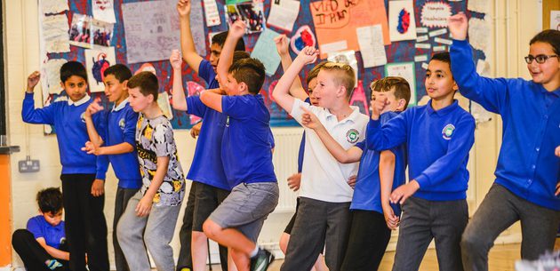 WNO Schools Workshops Kirsten McTernam A gruup of school children arms raised in play or performance.