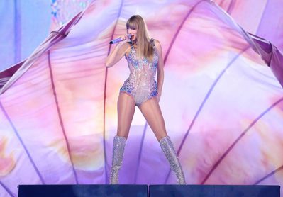 Taylor Swift - Credit Getty Images Taylor Swift stands on a podium holding a microphone to her mouth.