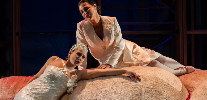 Lulu Photo Lulu, who wears a long white dress covered in sequins and a headpiece made of white leaves, lies across some large rocks as she sings. She holds a revolver in one hand. Above, Countess Geschwitz, who wears a white suit jacket and a matching skirt, sits on the rocks, looking down at Lulu with adoration.