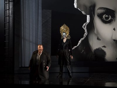 La Forza Del Destino Gwyn Hughes Jones Don Alvaro And Justina Gringyté Preziosilla Photo Credit Richard Hubert Smith 3650 Richard Hubert-Smith 2018 Man kneels front of stage while woman with large gold headdress on stands behind him.