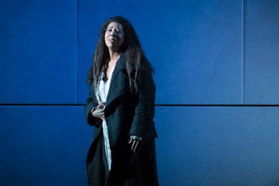La Forza Del Destino Mary Elizabeth Williams Donna Leonora Photo Credit Richard Hubert Smith 6058 Richard Hubert-Smith 2018 Woman stands with hand to her stomach looking pained, blue background.