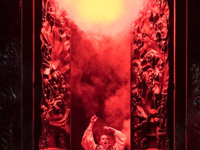 WNO Don Giovanni Gavan Ring Don Giovanni Photo Credit Richard Hubert Smith 2295 Richard Hubert-Smith 2018 Man on his knees with arms in the air looks distressed with red smokey background.