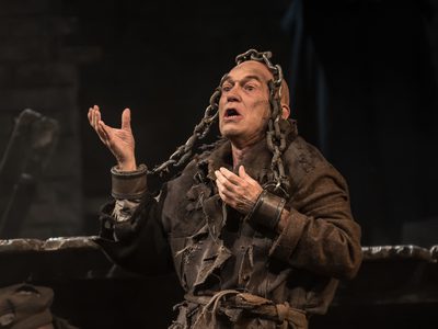WNO From The House Of The Dead Alan Oke Skuratov Photo Credit Clive Barda 0066 Clive Barda A man (Skuratov) stands with his mouth open, arms cuffed, in chains.