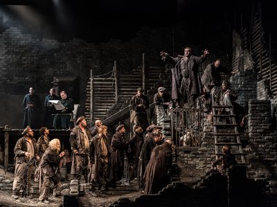 WNO From The House Of The Dead From The House Of The Dead Cast Photo Credit Clive Barda 0034 Clive Barda On a grey and atmospheric set, ten men stand chained at the bottom of some steps.