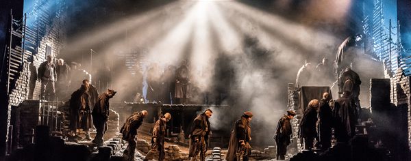 WNO From The House Of The Dead From The House Of The Dead Cast Photo Credit Clive Barda 0343S Clive Barda A dozen men wearing dark clothes walk somberly in line, across the dimly lit stage