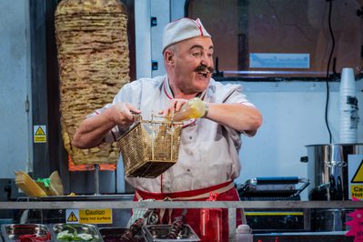 WNO Don Pasquale Andrew Shore Don Pasquale Photo credit Robert Workman 016 Robert Workman 2019 Man cooking chips in uniform looking happy.