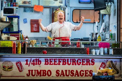 WNO Don Pasquale Andrew Shore Don Pasquale Photo credit Robert Workman 030 Robert Workman 2019 Man in fast food truck looking victorious with arms raised and tensed hands in fists.