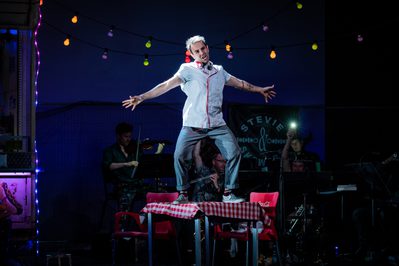 WNO Don Pasquale Nico Darmanin Ernesto Photo credit Robert Workman 040 Robert Workman 2019 Man in chefs outfit standing on table singing with arms outstretched.