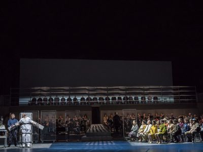 WNO Dead Man Walking Cast of Dead Man Walking Photo credit Johan Persson 03624 Johan Persson 2019 Wide shot of stage man strapped to gurney while others watch seated.