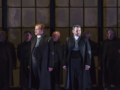 WNO Roberto Devereux George Newton Fitzgerald Page Robyn Lyn Evans Lord William Cecil Photo credit Bill Cooper 0107 Bill Cooper 2019 Man in formal coats gather in front of dark window.