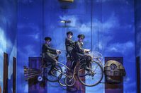 WNO The Magic Flute Cameron Lewis First Boy Ruby Llewelyn Third Boy Luke Samra Second Boy Photo Credit Bill Cooper 0380 Bill Cooper 2019 Three boys on bikes with fish head and tale cycling through the air.