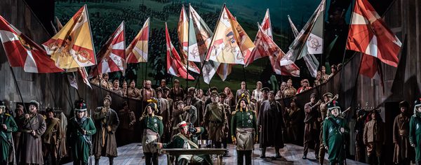 WNO War and Peace WNO Cast of War and Peace Photo credit Clive Barda 0391 Clive Barda Full cast are wearing smart uniforms, holding and waving a multitude of flags in the air.