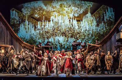 WNO War and Peace WNO Chorus Photo credit Clive Barda 0063 Clive Barda Full chorus are dancing under a ceiling filled with gold and white chandeliers.