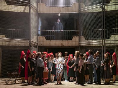 WNO Carmen Giorgio Caoduro Escamillo Julia Mintzer Carmen Photo credit Richard Hubert Smith 3917 Richard Hubert-Smith 2020 A woman is central focus with crowds around her and man watching from balcony above.