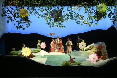 Production Image The Cunning Little Vixen Photocredit Richard Hubert Smith 0578 Richard Hubert-Smith 2019 Wide shot of stage large flowers and leaves and green hills.