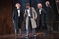 WNO Rigoletto 2019 Alastair Moore Marullo and Mark S Doss Rigoletto Photocredit Richard Hubert Smith 3709 Richard Hubert-Smith 2019 Man in trench coat surrounded by 3 figures in clown figures.