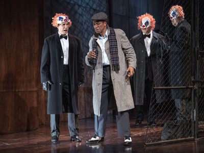 WNO Rigoletto 2019 Alastair Moore Marullo and Mark S Doss Rigoletto Photocredit Richard Hubert Smith 3709 Richard Hubert-Smith 2019 Man in trench coat surrounded by 3 figures in clown figures.