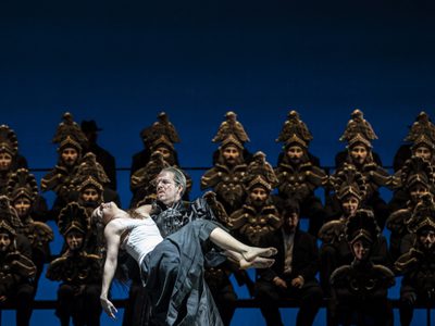 WNO Marine Tournet as Dancer and Giorgio Caoduro as Guy de Montfort in Les vêpres siciliennes PHOTO CREDIT Johan Person 5970 Dancer being held by Guy de Montfort with chorus standing in background