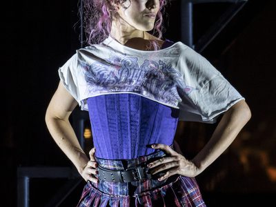 WNO Candide Claudia Boyle Cunégonde photo credit Johan Persson 10302 a woman with pink hair stands with her hands on her waist