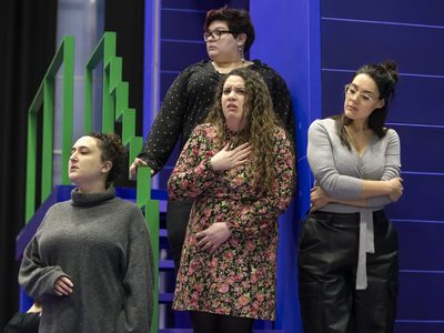 WNO The Magic Flute Cast of Magic Flute photo credit Craig Fuller 5444 A group of women stand on a set of blue stairs, looking judgementally to the left