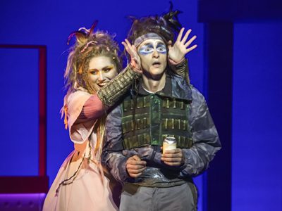 WNO The Magic Flute Jenny Stafford Papagena Quirijn de Lang Papageno photo credit Craig Fuller 4961 A man in hunting equipment stands shocked whilst a women in a pink dress takes her hands from in front of his eyes