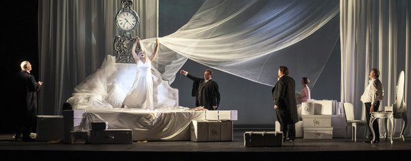 WNO The Makropulos Affair Cast of The Makropulos Affair photo credit Richard Hubert Smith 2148 Large white bedroom, with a sheer curtain held above the bed by a standing woman