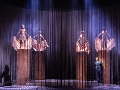 Hanna Hipp as Federico García Lorca and Ensemble in WNO Ainadamar 2023 Credit Johan Persson 07324 four women stand on pillars, holding their shawls behind them