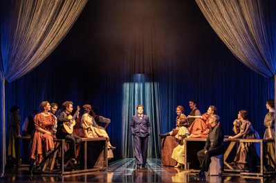 Hanna Hipp as Federico García Lorca in WNO Ainadamar 2023 Credit Johan Persson 06243 a woman in a suit walks forwards in a bar scene, as the patrons observe them