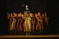 Jaquelina Livieri as Margarita Xirgu Julieth Lozano Rolong as Nuria in WNO Ainadamar 2023 Credit Johan Persson 02408 A woman in a black dress stands lit up in the background, as in the foreground a group of women hold their right hands to the sky