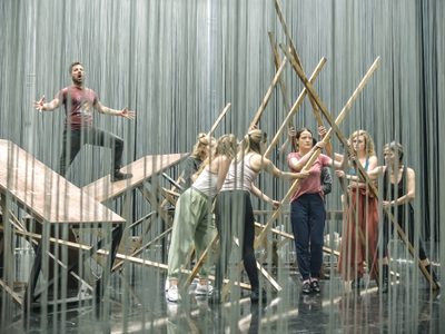 WNO Ainadamar Hanna Hipp Federico García Lorca cast of Ainadamar photo credit Craig Fuller 4975 a group of performers arrange beams of wood into a triangular tunnel, as a man stands on two tables