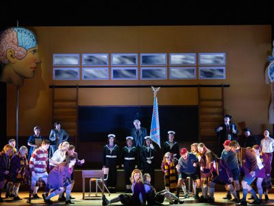 WNO Così fan tutte Cast of Così fan tutte photo credit Elliott Franks 3125 A production image of Cosi fan tutte. Cast and chorus are on stage and dressed in purple
