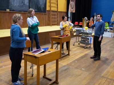 WNO Così fan tutte Sophie Bevan Fiordiligi Kayleigh Decker Dorabella Rebecca Evans Despina Max Hoehn Director photo credit Elliott Franks 5443 A rehearsal shot of four characters stood around school desks