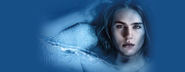WNO CL1881 S24 Website image 2000x785 Header Death in Venice A man with long hair looks at the character as he lies back with his arm next to his head against a blue background