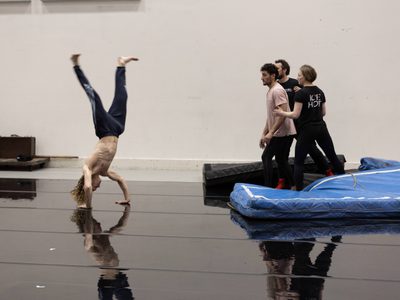 WNO Death in Venice Antony Cesar Tadzio Riccardo Saggese Governess and Cast of Death in Venice photo credit Craig Fuller 0834 A rehearsal shot showing a shirtless man in a handstand as three men look on