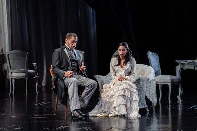 WNO La traviata Mark S Doss Giorgio Germont Stacey Alleaume Violetta photo credit Julian Guidera 9 An older gentleman in a suit talks to a young woman in a white dress, both are seated