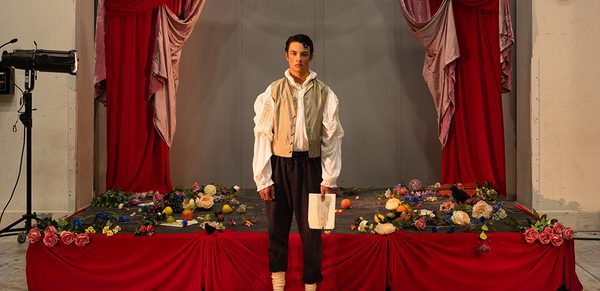 WNO 2627 Launch AL Cover A man stands in front of a red stage covered in flowers. He's holding a white piece of paper.