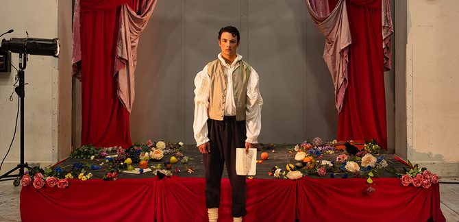 WNO 2627 Launch AL Cover A man stands in front of a red stage covered in flowers. He's holding a white piece of paper.