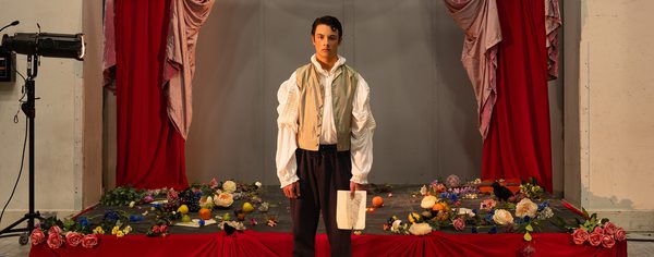 WNO 2627 Launch AL Header A man stands in front of a red stage covered in flowers. He's holding a white piece of paper.