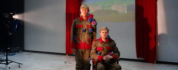 WNO 2627 Launch HW Header Two men dressed in army gear and flowers stand in front of a projected image of Trawsmynydd Nuclear Station.