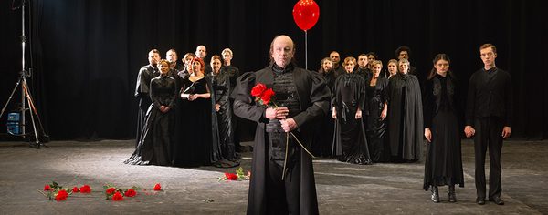 WNO 2627 Launch LB Cover A large group of people all dressed in black stand in the background. In the foreground, two lovers, and a man holding a red balloon and flowers