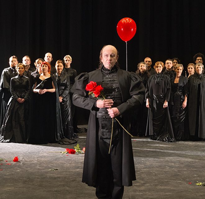WNO 2627 Launch LB Cover A large group of people all dressed in black stand in the background. In the foreground, two lovers, and a man holding a red balloon and flowers