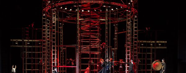WNO Lulu Photo Credit Clive Barda 0009 Clive Barda Animals and humans are in an elaborate metal prison cage. The stage is is dimly lit, with red lighting.